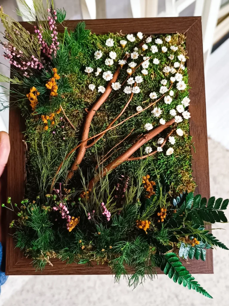 Cuadro de musgo preservado con ramas, flores blancas y marco de nogal
