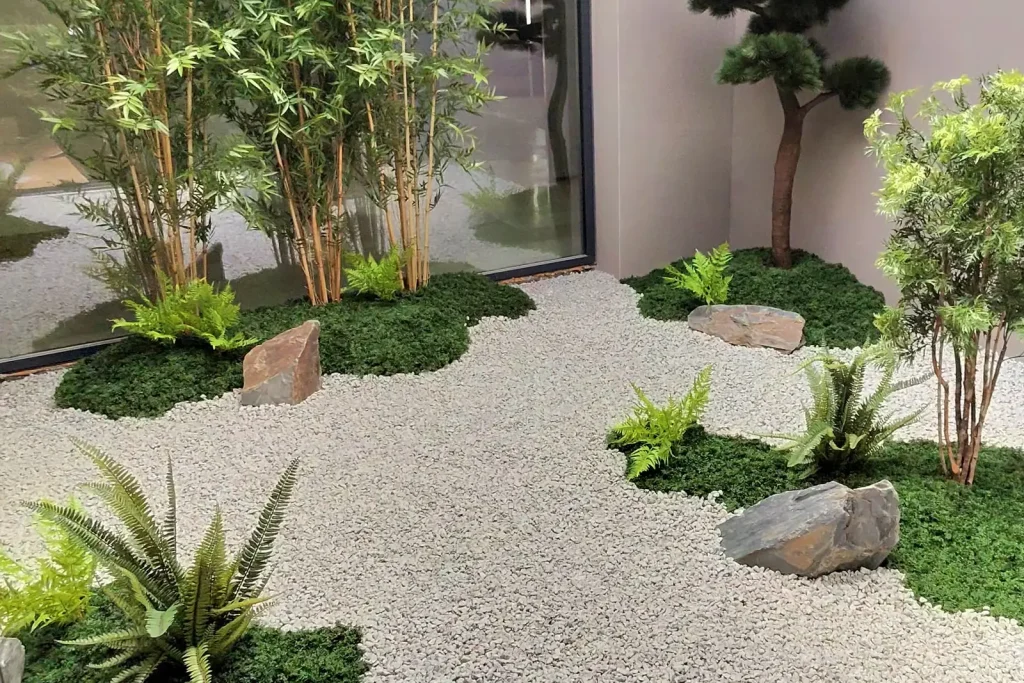 Patio interior de oficina con bambú, helechos, rocas y grava blanca