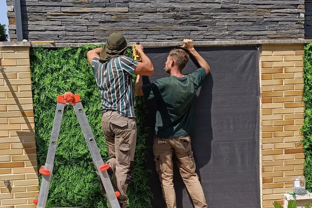 Dos operarios de espaldas fijando un jardín vertical sobre un muro de ladrillo