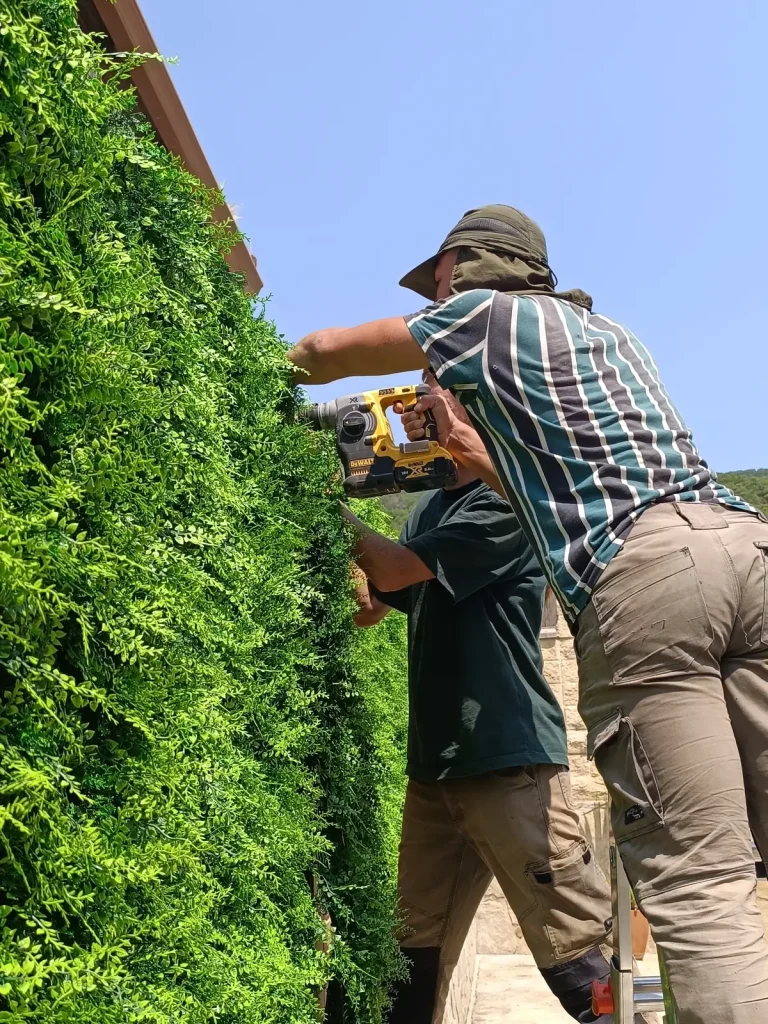 Operario atornillando con taladro los paneles de un jardín vertical en una fachada