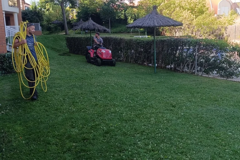 Dos jardineros segando el césped con tractor cortacésped y recogiendo una manguera