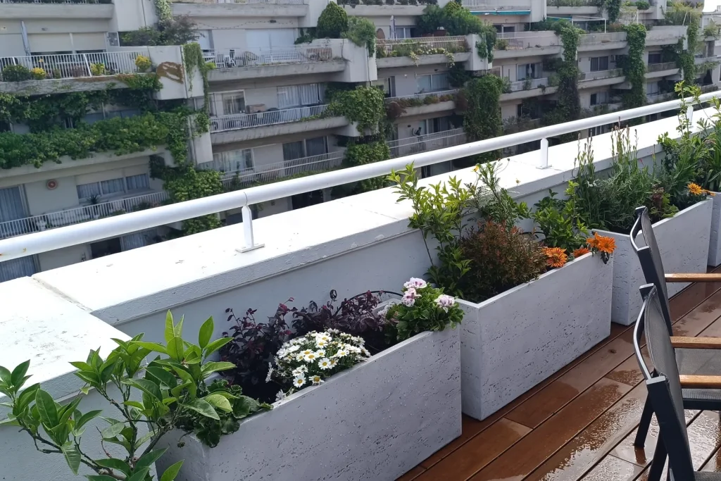 Jardineras blancas con flores y arbustos sobre tarima de madera en un ático